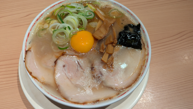 どんぶりの周囲に刻みネギ、チャーシュー、のり、チャーシューが3枚あり、真ん中に卵黄が載せてあるラーメン