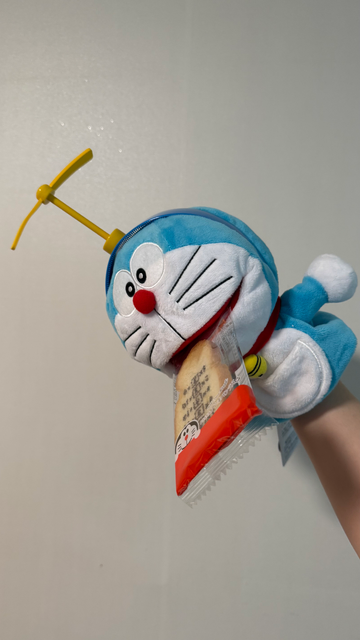 ドラえもんのパペット縫い包みがアンキパンを口にしたままタケコプターに乗っている。